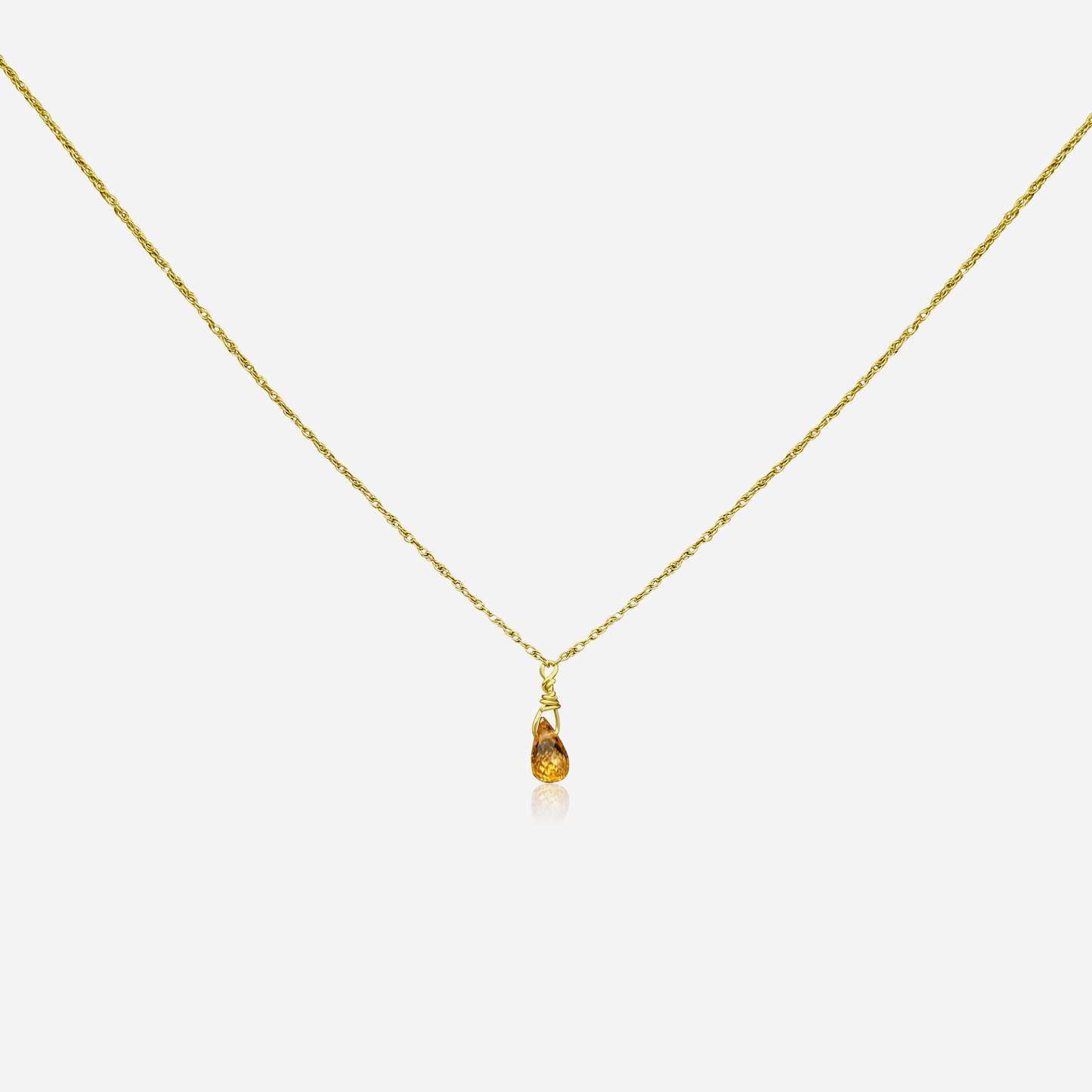 A gold-colored necklace with a teardrop-shaped orange pendant at the end, displayed against a white background.