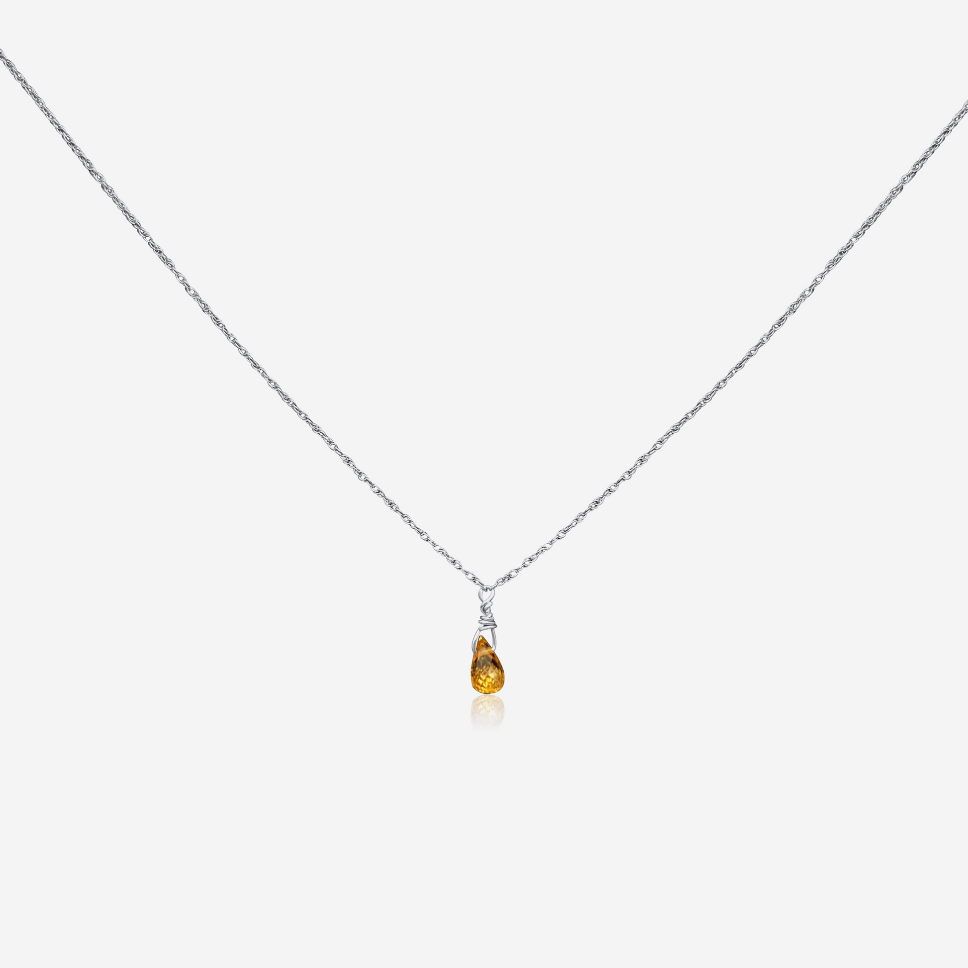 A gold-colored necklace with a teardrop-shaped orange pendant at the end, displayed against a white background.