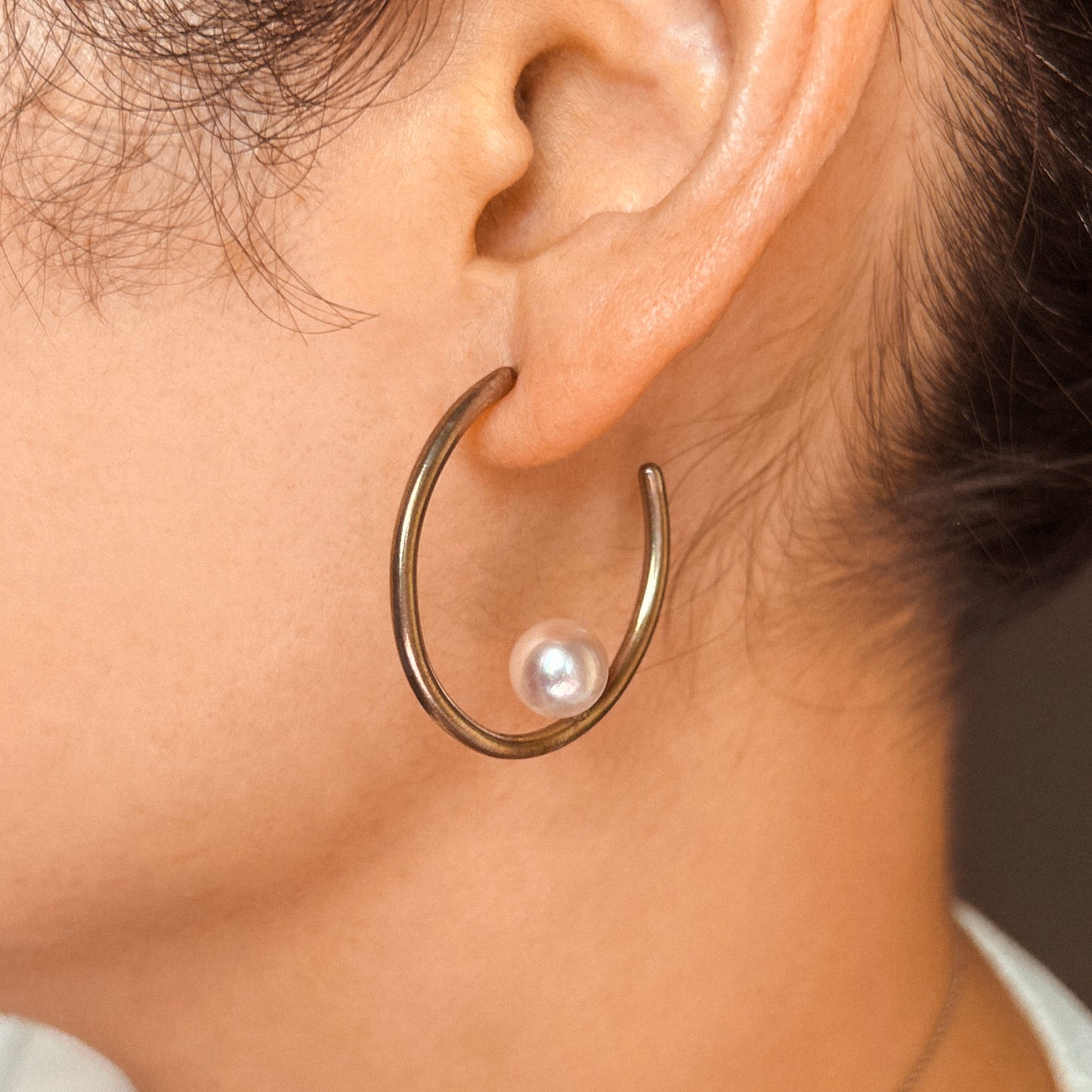 A pair of hoop earrings with Akoya pearls set within the hoops, displayed against a white background.
