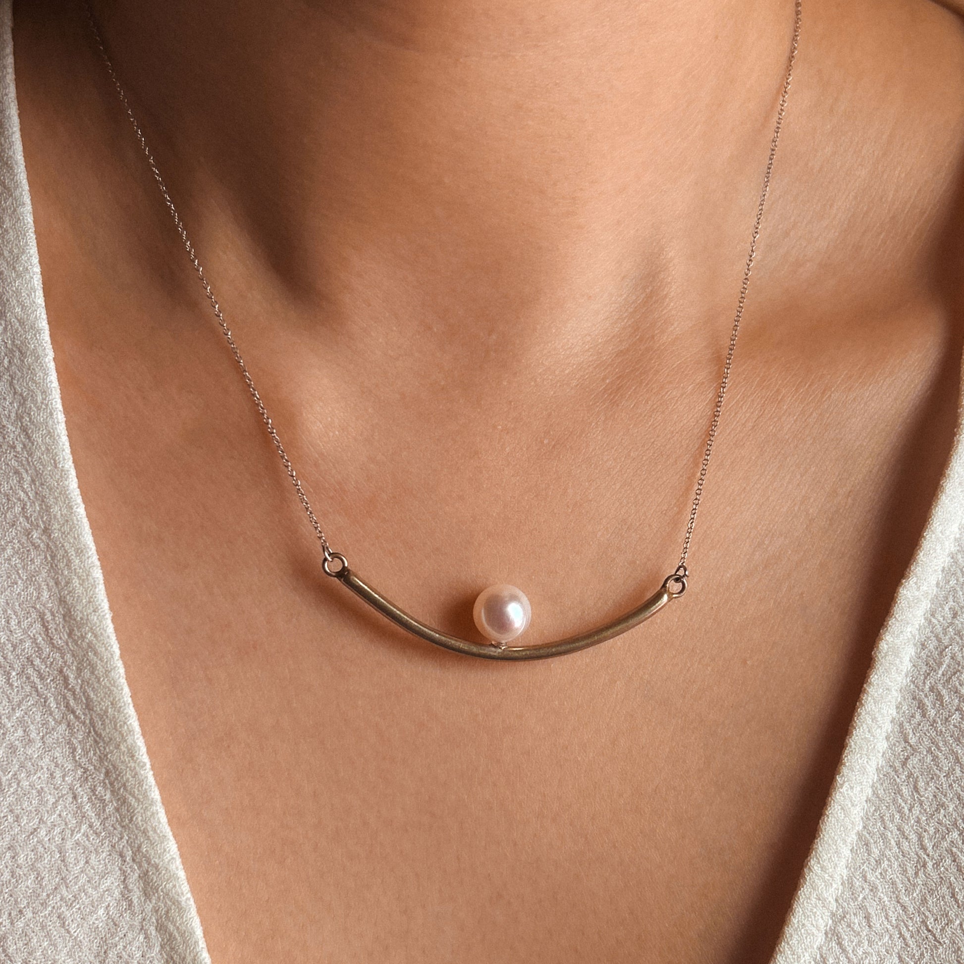 A tube-shaped pendant necklace with an Akoya pearl elegantly placed in the center, hanging from a delicate chain.