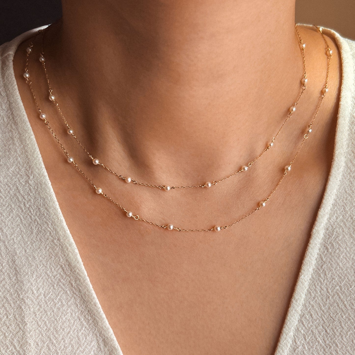 A delicate Tiny Akoya Pearl Necklace with small pearls on a gold-tone chain displayed against a white background.