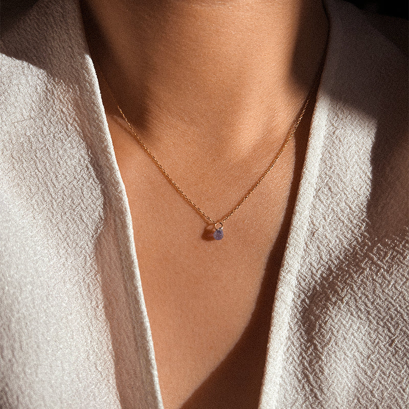 A single Tanzanite drop necklace on a gold chain against a white background.