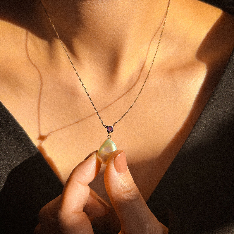A gold-tone necklace featuring a drop-shaped freshwater pearl pendant with smaller amethyst beads above it on a white background.