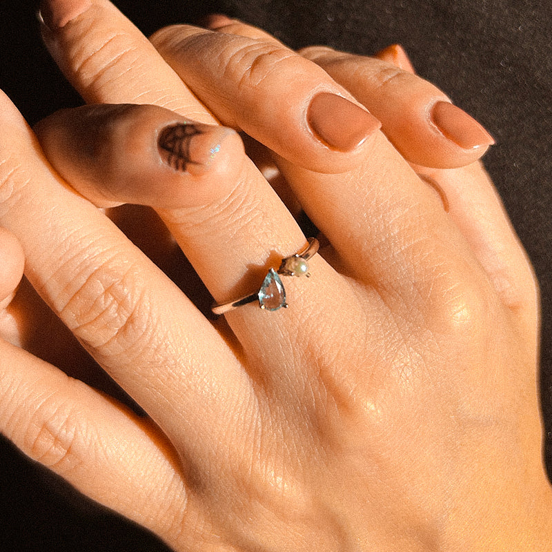 Close-up of a hand wearing two rings with gemstones on a dark background