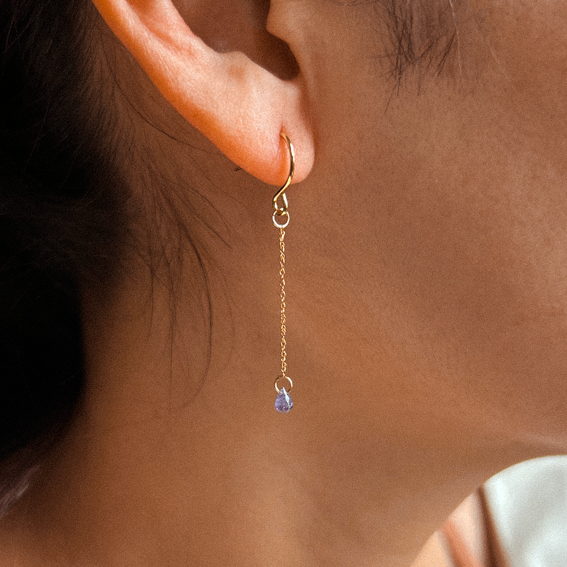 Gold earring with a blue gemstone worn by a person