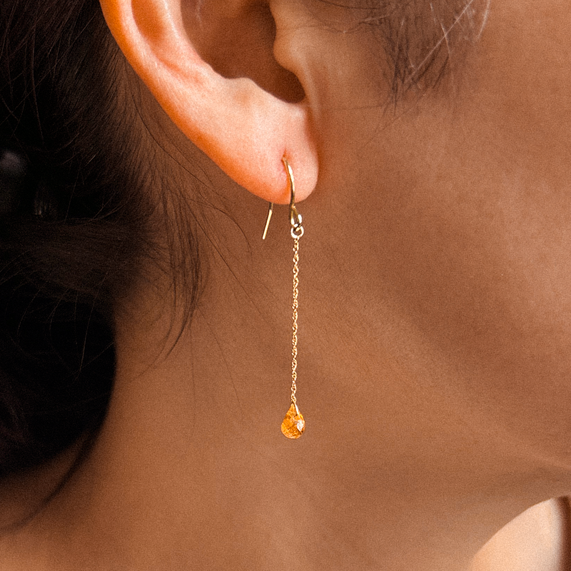 Close-up of a person wearing a gold chain earring with a small yellow gemstone.