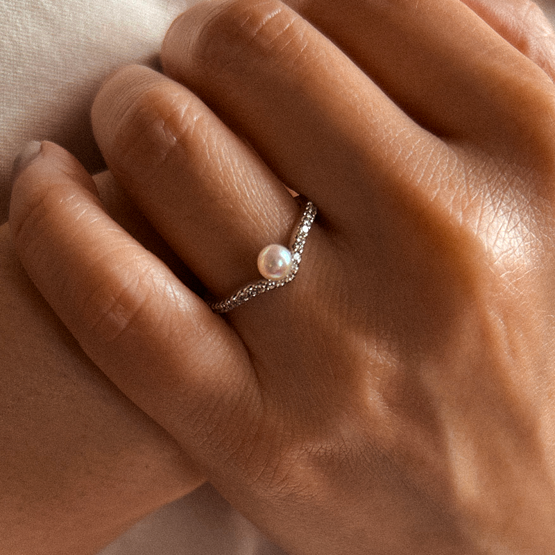 Close-up of a hand wearing a pearl ring with a soft background