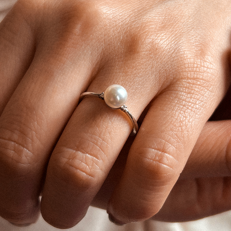 Pearl ring on a finger with a soft focus background