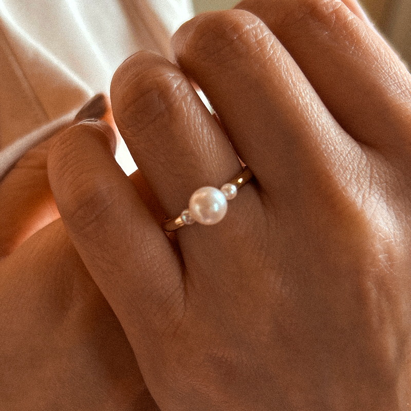 Close-up of a hand wearing a pearl ring with a blurred background