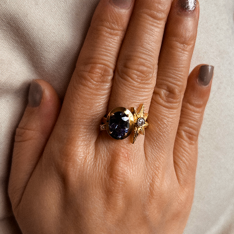 Gold ring with a dark gemstone on a hand against a neutral background
