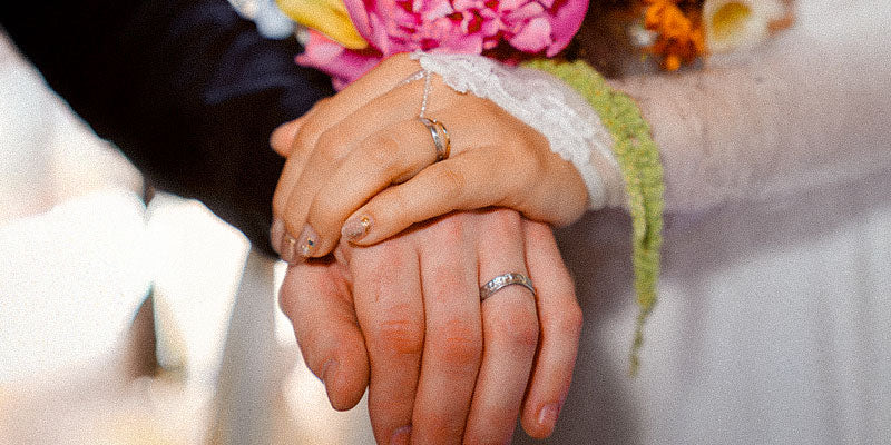 Two hands holding each other with wedding rings, blurred background